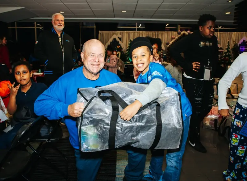 A volunteer and a smiling student carry a big bag of gifts