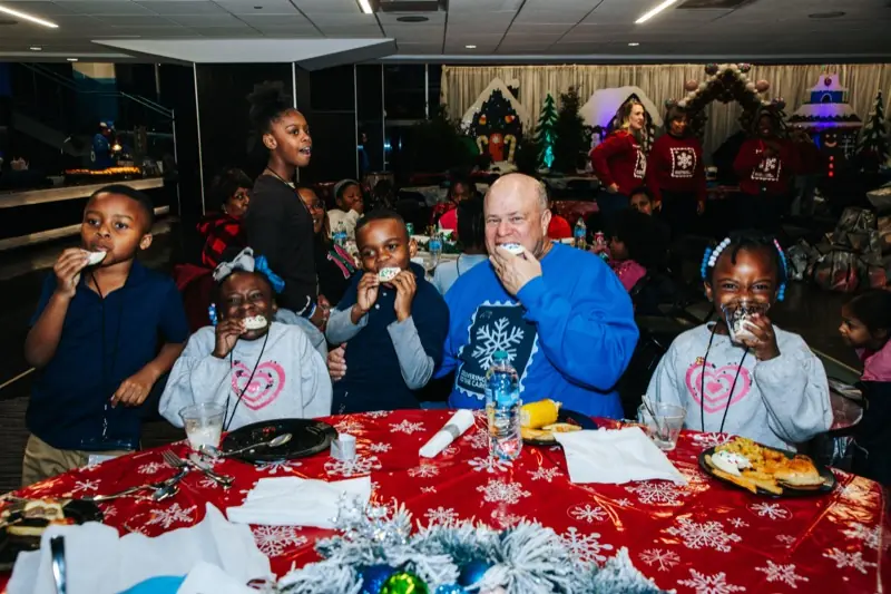 Students and a volunteer share cookies at a festive red table