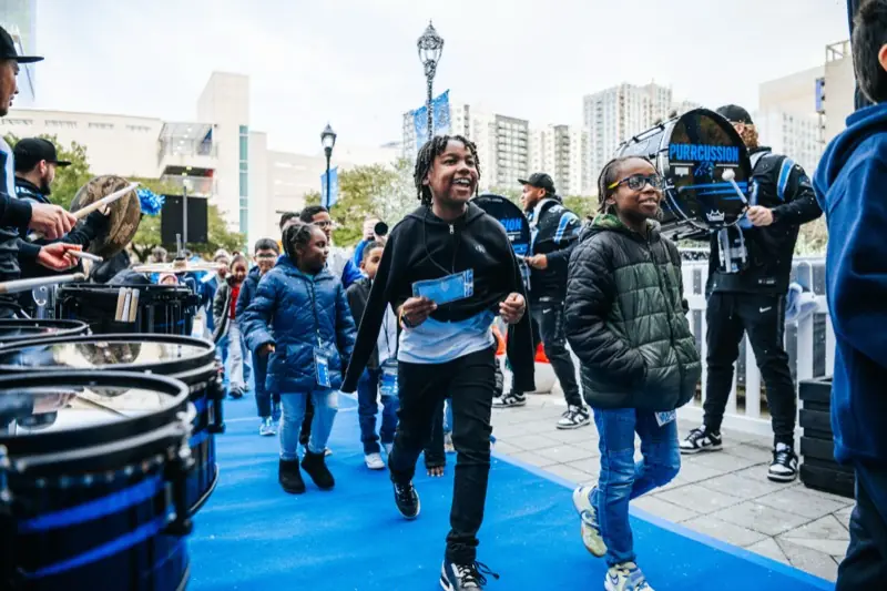 Students walk a blue carpet past the PURRcussion drumline